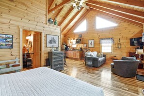 A spacious log cabin with a high ceiling, a cozy living area with a sofa and armchairs, a kitchen, and a large bed.