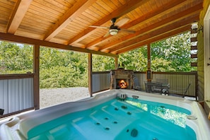A hot tub with a stone fireplace and outdoor furniture under a wooden pergola.