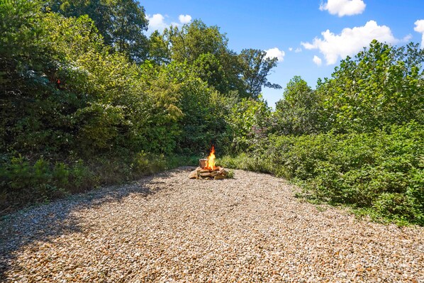 Ein Kiesweg führt zu einem Lagerfeuer in einem bewaldeten Gebiet.