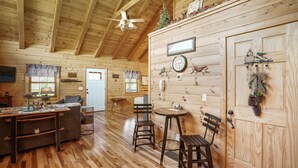 A cozy cabin interior with wooden walls, a dining area with a table and chairs, a kitchen area, and a living room with a sofa and a television. - Lovebirds Landing | Hocking Hills, Couples Cabin (Logan)