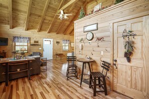 Ein gemütliches Blockhäuschen-Interieur mit Holzwänden, einem Essbereich mit Tisch und Stühlen sowie einem Deckenventilator.