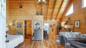 A cozy cabin interior with a bed, a sofa, a dining table, and a kitchen area. - Lovebirds Landing | Hocking Hills, Couples Cabin (Logan)