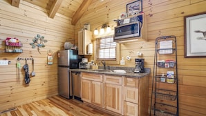 A compact kitchen with wooden cabinets, a stainless steel refrigerator, a microwave, and a coffee maker. - Lovebirds Landing | Hocking Hills, Couples Cabin (Logan)