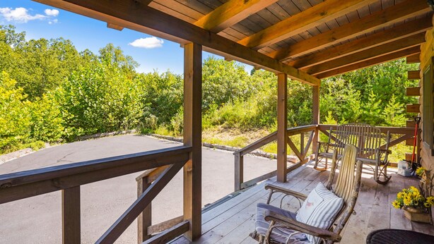 A wooden deck with a bench and a chair, overlooking a parking area and dense greenery. - Lovebirds Landing | Hocking Hills, Couples Cabin (Logan)