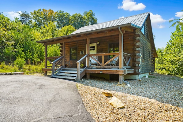 A log cabin with a porch, steps, and a gravel driveway.