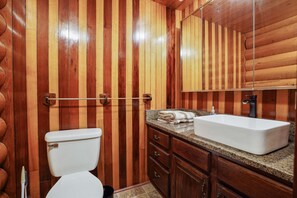 A wooden-paneled bathroom with a white toilet, a granite countertop, and a large mirror. - Diamond In The Rough | Waterfall & Rock Wall (Rockbridge)