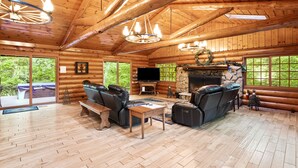 L’intérieur d’une cabane en rondins, avec une cheminée, des canapés en cuir, un téléviseur et de grandes fenêtres.