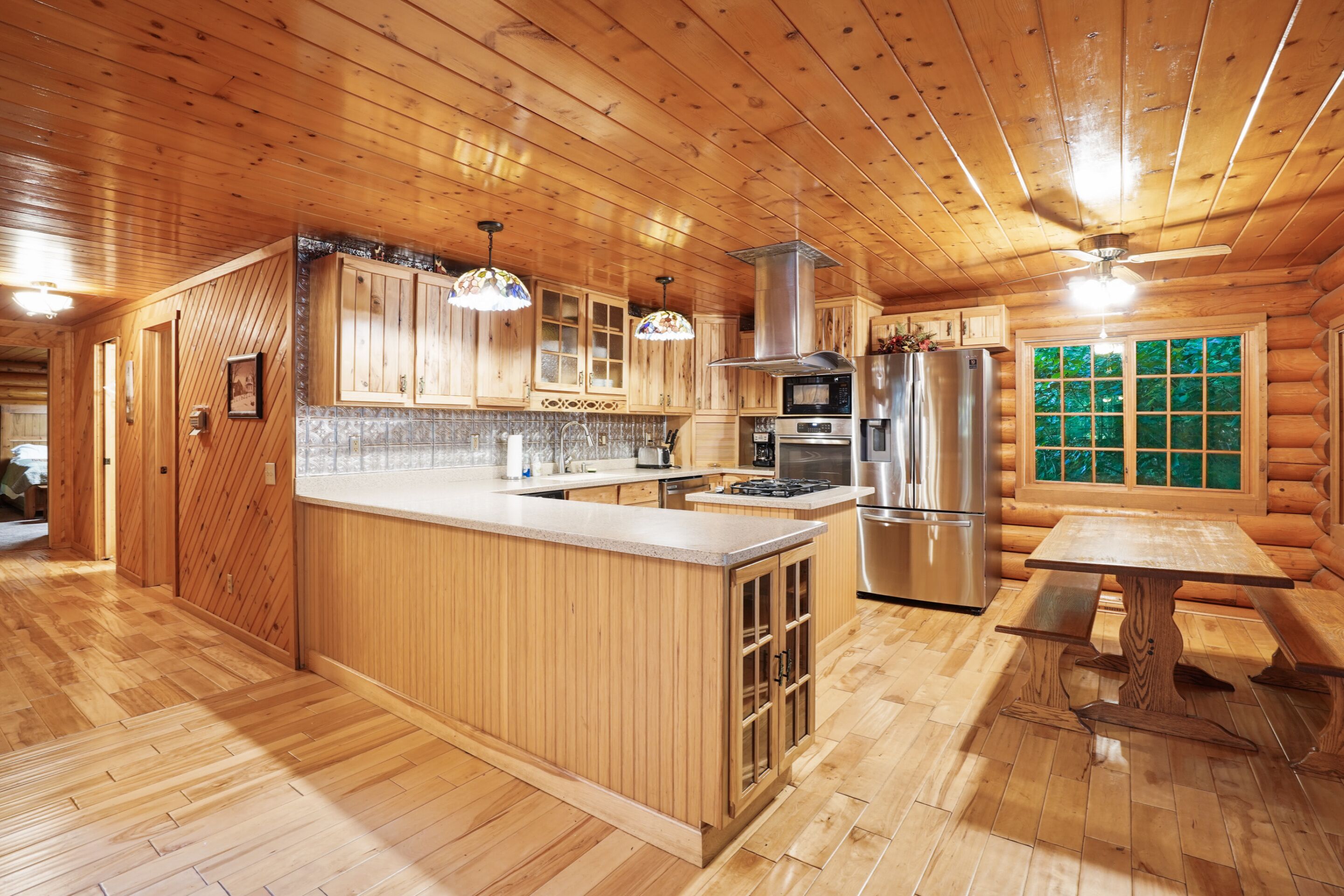 A wooden cabin interior with a kitchen, dining area, and a large window with a view.