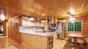 A wooden cabin interior with a kitchen, dining area, and a large window with a view. - Diamond In The Rough | Waterfall & Rock Wall (Rockbridge)