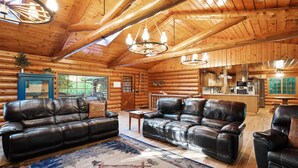 A log cabin interior with leather sofas, a dining area, and a kitchen. - Diamond In The Rough | Waterfall & Rock Wall (Rockbridge)