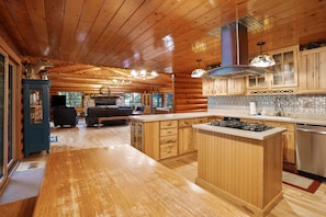Un intérieur spacieux de chalet en bois, avec une cuisine centrale dotée d’un îlot, des armoires en bois et une cheminée.