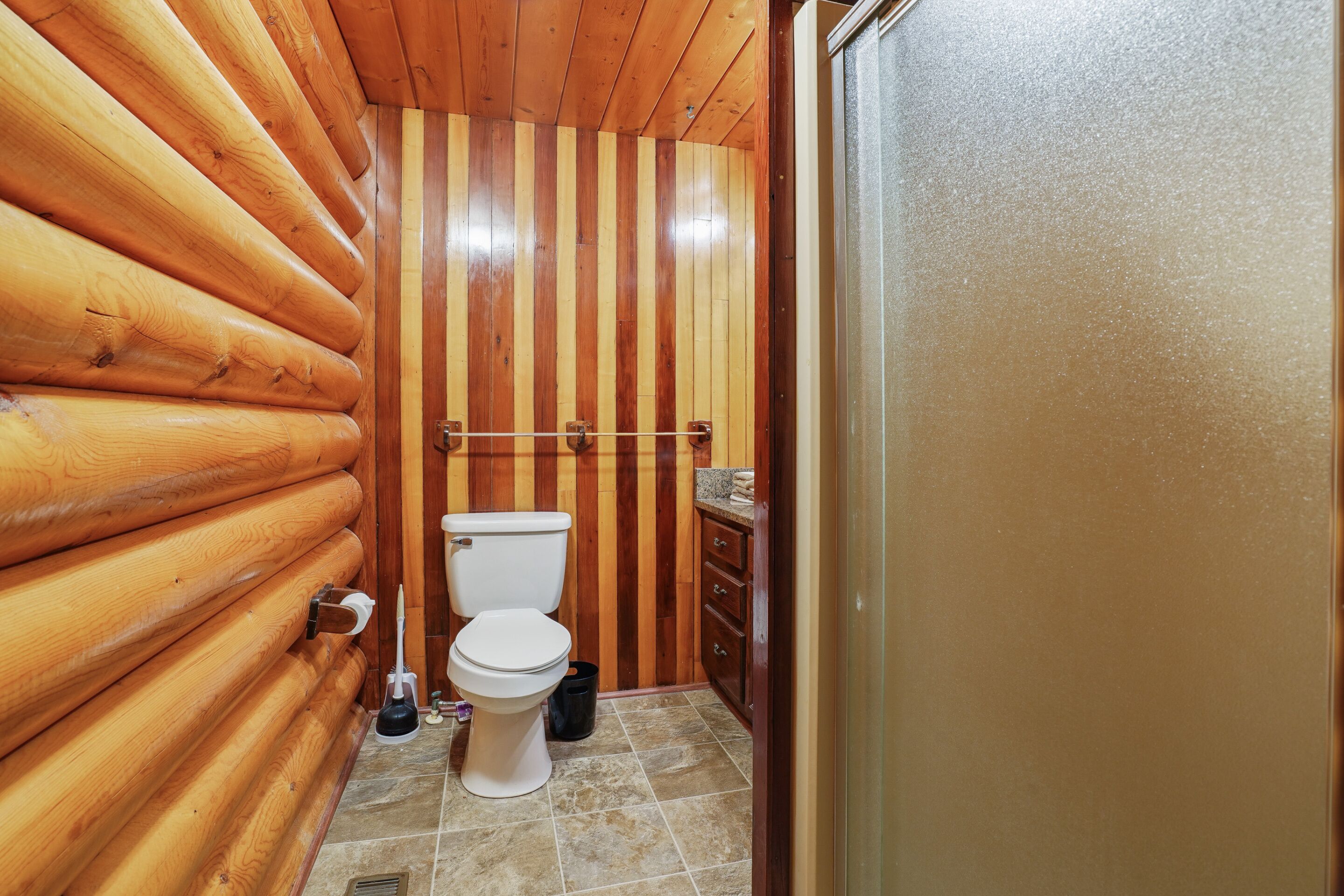 A wooden-paneled bathroom with a toilet, a sink, and a towel rack.