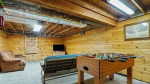 Une pièce chaleureuse avec un décor en bois, un baby-foot, un canapé et un téléviseur.