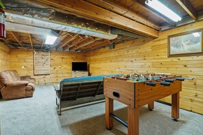 A cozy room with a wooden interior, a foosball table, a sofa, and a television.
