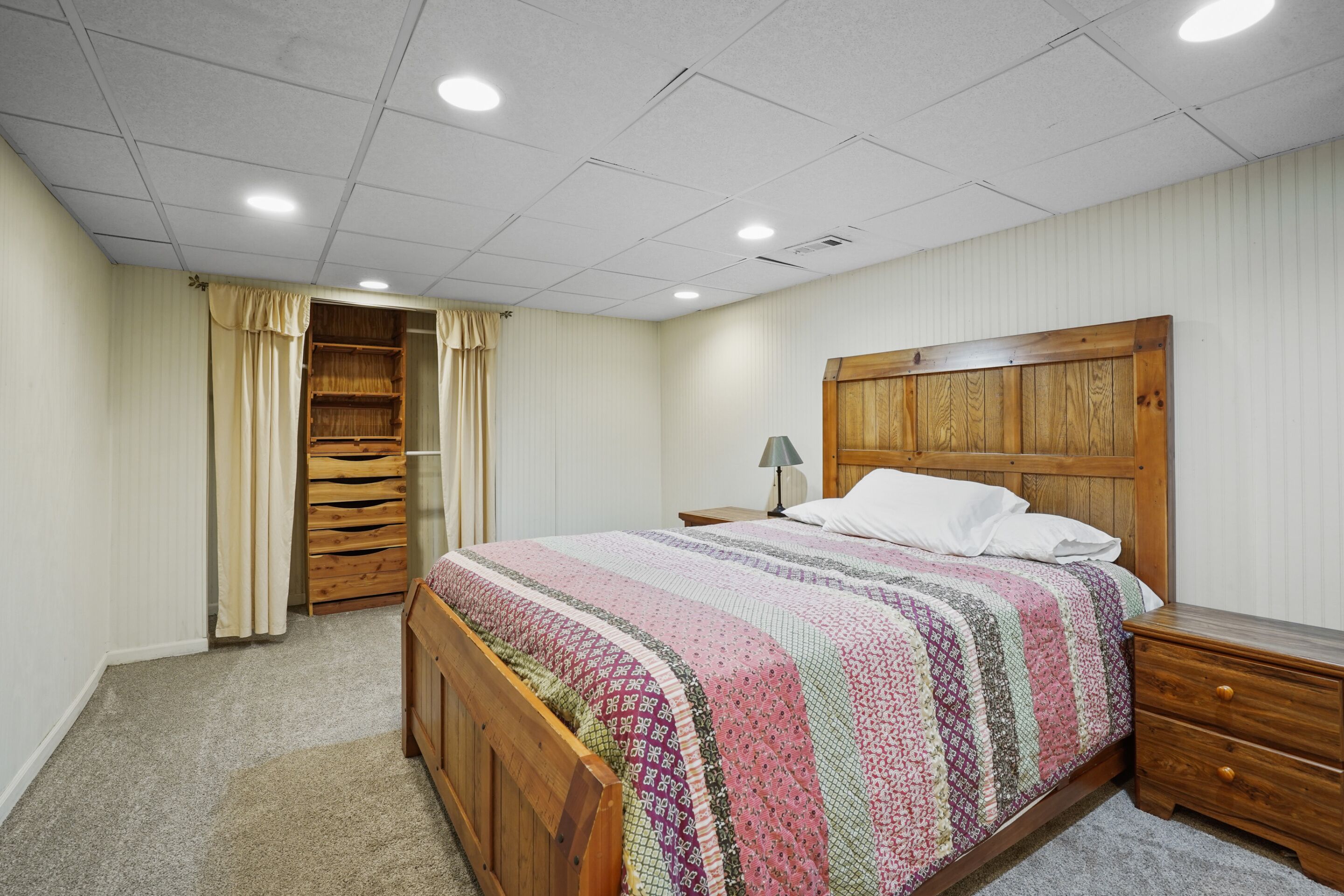 Un dormitorio con una cama de madera, una mesita de noche, una lámpara, un armario y una ventana con cortinas.