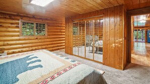 A log cabin interior with a large bed, a sliding glass door leading to a balcony, and a window with a view of greenery. - Diamond In The Rough | Waterfall & Rock Wall (Rockbridge)