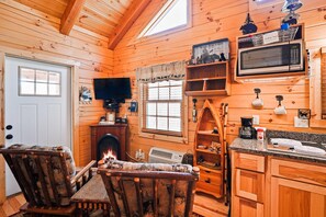A cozy cabin interior with a fireplace, wooden furniture, a television, and a kitchen area.