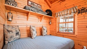 Una habitación de cabaña de madera con una cama, un estante con un peluche de oso y una ventana con un cartel que dice 'BIENVENIDOS'.