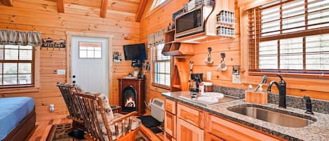 Interior de una cabaña de troncos con chimenea, muebles de madera, una cocina con encimeras de granito y un televisor.