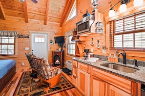 A log cabin interior with a fireplace, wooden furniture, a kitchen with granite countertops, and a television. - Snuggle Bear | Hocking Hills, Adorable Tiny Home (Logan)