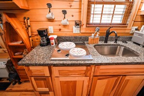 A kitchen with wooden cabinets, granite countertop, stainless steel sink, coffee maker, and decorative plates. - Snuggle Bear | Hocking Hills, Adorable Tiny Home (Logan)