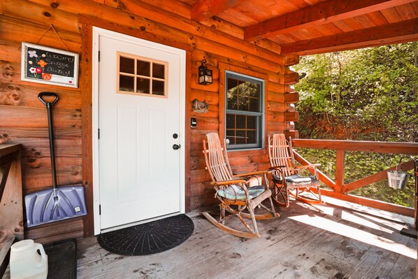 A wooden cabin with a white door, a rocking chair, a table, and a window.