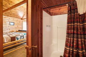 Ein Holzhütten-Interieur mit einem Bett, einer zur Dusche führenden Tür und einem gemusterten Vorhang.