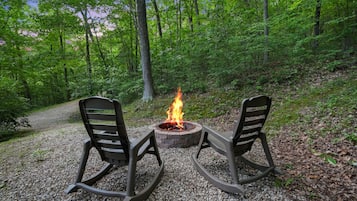 A forest setting with a fire pit and two chairs.