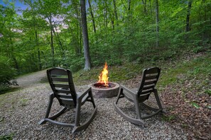 Waldlandschaft mit Lagerfeuer und zwei Stühlen.