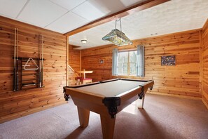 A pool table in a room with wooden walls and a hanging light fixture.