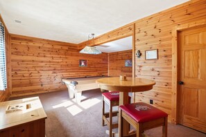 Ein Zimmer mit Holzwänden, einem Billardtisch, einem Billardkühler und einem kleinen Tisch mit Hocker.