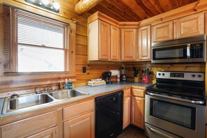 A kitchen with wooden cabinets, stainless steel appliances, a dishwasher, and a window with blinds.