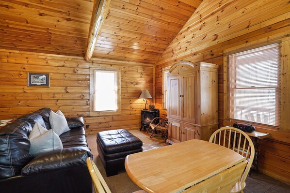 A cozy cabin interior with a leather sofa, wooden dining table, and a fireplace.