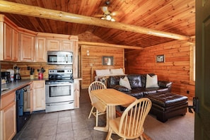 A cozy cabin interior with wooden walls, a kitchenette, a leather sofa, and a dining area.