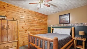 A wooden-framed bed with a headboard, a wooden wardrobe, and a small table with a lamp. - White Oak Cabin | Hocking Hills, Hot Tub, Rec Room (Rockbridge)