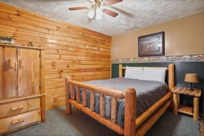 A wooden-framed bed with a headboard, a wooden wardrobe, and a small table with a lamp. - White Oak Cabin | Hocking Hills, Hot Tub, Rec Room (Rockbridge)