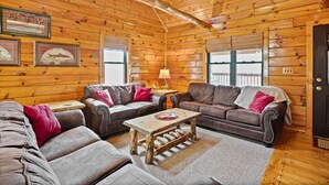 A log cabin interior with two leather sofas, a wooden coffee table, and framed pictures on the walls. - White Oak Cabin | Hocking Hills, Hot Tub, Rec Room (Rockbridge)