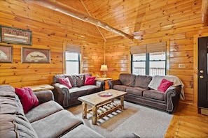 A log cabin interior with two leather sofas, a wooden coffee table, and framed pictures on the walls. - White Oak Cabin | Hocking Hills, Hot Tub, Rec Room (Rockbridge)