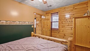 Une chambre avec un lit, des murs en bois, un ventilateur de plafond et une fenêtre donnant sur un beau paysage.