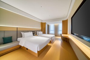 Habitación de hotel con dos camas, una zona de estar, un escritorio y una pantalla grande.