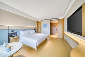 Una habitación de hotel moderna con una cama grande, mesitas de noche, un escritorio y una televisión.