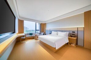 Una habitación de hotel moderna con una cama grande, un escritorio, una silla, una mesita y vistas a la ciudad.