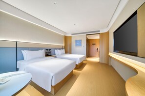 Habitación de hotel con dos camas, un escritorio, un televisor y una puerta que da a un pasillo.