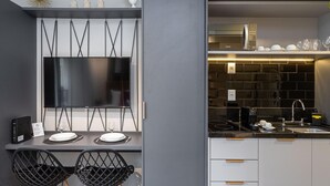 A modern kitchen with a flat-screen TV mounted on a wall, a dining area with two chairs, and a built-in stove. -  Charlie Alves Guimarães Pinheiros (São Paulo)