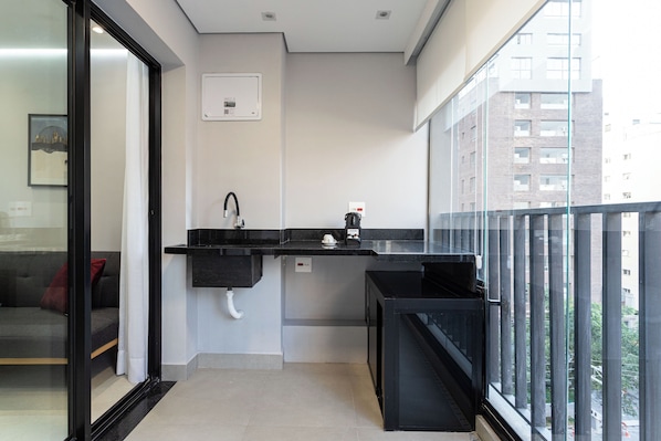 A compact balcony with a black sink, a small coffee machine, and a view of a cityscape through large windows.