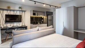 A modern bedroom with a large bed, a TV, a kitchenette, and a wardrobe. -  Charlie Alves Guimarães Pinheiros (São Paulo)