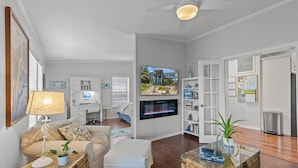 A spacious living room with a fireplace, a television mounted on the wall, and a bookshelf. - Kiss Me Kottage- Private Waterfront Home! (Cedar Key)