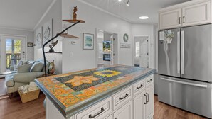 A modern kitchen with a large island, stainless steel appliances, and a unique mosaic backsplash. - Kiss Me Kottage- Private Waterfront Home! (Cedar Key)