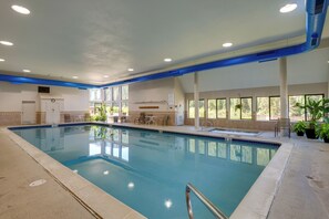 Una piscina interior con agua azul cristalina, rodeada por una terraza con baldosas y algunas plantas en macetas.