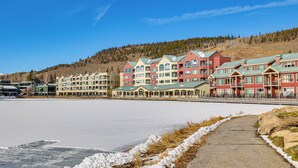 A row of multi-story buildings with balconies, a frozen lake in the foreground, and a hilly landscape in the background. - Keystone Lake Haven: Heated Pool & Ski Shuttle! (Keystone)